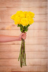 Women hand holding a bouquet of peach Stardust roses variety, studio shot. Yellow flowers