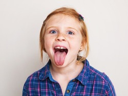 Happy redhead little girl in blue plaid shirt showing her tongue.