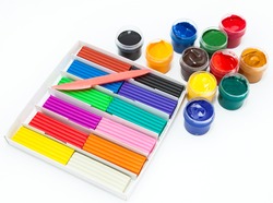 Cardboard box with colorful plasticine bars, plastic knife and color paints in bottles, a white background
