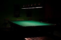 An empty billiard table, bathed in lamplight against a dark background.