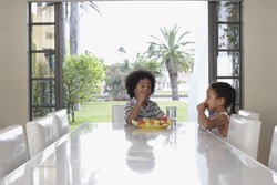 Little boy and girl eating fruit salad at dining table