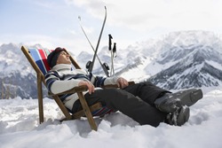 Side view of a man in warm clothing resting on deckchair in snowy mountains