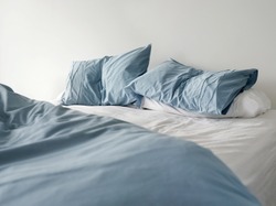 Morning view of an unmade bed with crumpled blue bed linens and no people