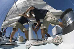 Low angle view of sailors operating windlass on yacht
