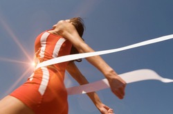 Low angle view of young female athlete crossing finish line against clear blue sky