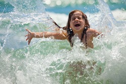 Little girl laughing and crying in the spray of waves at sea on a sunny day