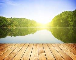 Sunset on forest lake and wooden board background