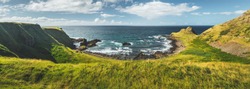 Panoramic overview of the Northern Ireland shoreline. Amazing Irish landscape. Green grass covered shore surrounded by the ocean water. Cozy bay under the cloudy sky background. Wilderness.