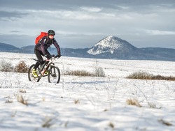 Mountain extreme biker in snowy landscape. Sportsman properly equiped for winter cycling is ridding in heavy terrain.  Sunny winter weather and snow.