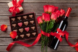 Valentines day with red roses, wine bottle and chocolate box on wooden table. Top view