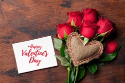 Valentine's day greeting card with red rose flowers bouquet and knitted heart on wooden background. Top view with space for your greetings