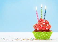 Birthday cupcake with three burning candles over blue background with copy space for your greetings