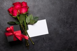 Valentines day greeting card with red rose flowers bouquet and gift box on stone table. Top view flat lay with space for your greetings