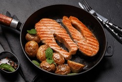 Grilled salmon steaks and potatoes sizzling in a frying pan