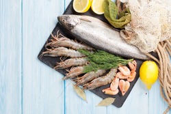 Fresh raw sea food with spices on stone plate over wooden table background. Top view with copy space