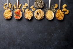 Various pasta on spoons over stone background. Top view with copy space