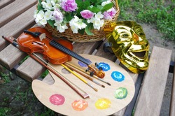 Attributes of the arts. Art palette, brushes, violin, bow, theater mask, a bouquet of roses and jasmine on a garden bench.