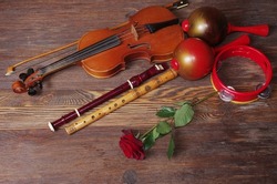 Acoustic guitar, violin, pipes, maracas, tambourine and red rose on a wooden table.