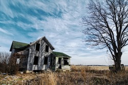 Photo of an old scary abandoned farm house that is deteriorating with time and neglect.  Enhanced with an old tree and a hangman's noose topped off with a dramatic  sky.