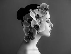 Portrait of beautiful young woman with orchid. Brunette woman with luxury makeup. Eyelashes. Cosmetic eyeshadow. Black and White photo