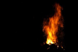 Amazing bonfire with beautiful yellow and orange spurts of flames and a huge sheaf of sparks in the form of tracks on a black background