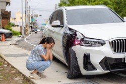 Frightened woman sits in front of crashed car