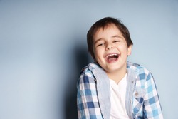 Portrait of happy joyful laughing beautiful little boy on blue background
