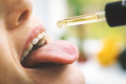 herbal alternative medicine and dietary supplements - woman taking cbd hemp oil drops in mouth from dropper. medical cannabis