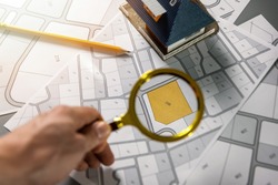 searching building plot for family house construction - hand with magnifier on cadastre map