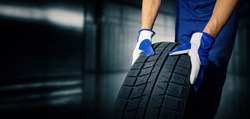 car tire shop and service - mechanic holding new tyre on garage background. copy space 