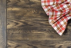 Checkered napkin at right top corner of oak table background, top view with copy space