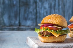 Hamburger with beef, cheese and vegetables on rustic table. Closeup with copy space
