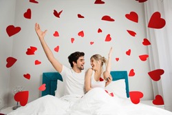 Young happy couple sitting on the bed, throwing red hearts 