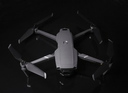 New dark grey drone quadcopter with digital camera and sensors flying isolated on black background
