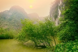 Vietnamese tropical nature (tropical winter). Forests and rocky cliffs of the mountains - narrow canyon of river. The setting of the foggy sun