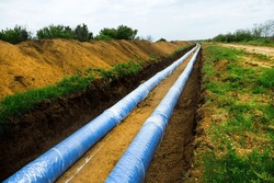 Construction of a water conduct. A double thread of large diameter water pipe is laid through plain fields, pipes in a trench