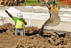 Construction contractor using a small track hoe excavator to dig a water line trench on a new commercial residential development