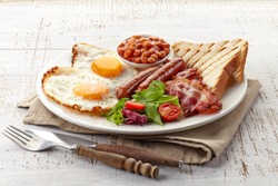 English breakfast with fried eggs, bacon, sausages, beans, toasts and fresh salad
