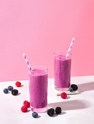 Two glasses of purple wild berry smoothie or milkshake on pink pastel background, copy space for text. Healthy breakfast drink