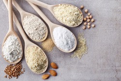 Wooden spoons of various gluten free flour (almond flour, amaranth seeds flour, buckwheat flour, rice flour, chick peas flour) from top view
