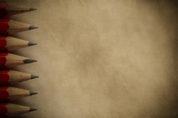 A column of pencil tips pointing inward, forming a border on the left side of a piece of parchment paper copy space with vignette.  Vintage style image for education or arts background.