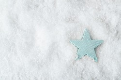 Overhead shot of a pale blue wooden star on artificial white snow background with copy space to the left. Christmas background.