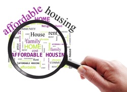 Hand with magnifying glass looking at Affordable Housing word cloud, on white background with copy space