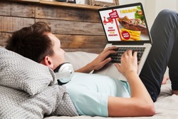 Man ordering take away food by internet with a laptop while lying at home.