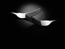 Two shiny stainless steel eating forks on shiny black background. Elegant food and beverage concept.
