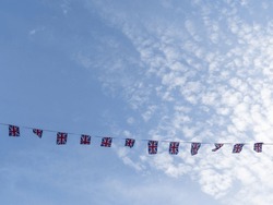 A line of small rectangular Union Jack bunting flags, stretched across a summer sky.
