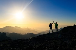Couple hikers celebrating success in sunset mountains, accomplish with arms up outstretched. Young man and woman looking at beautiful inspirational landscape view, Gran Canaria Canary Islands.
