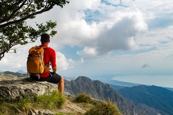 Man tourist hiker or trail runner looking at beautiful inspirational landscape in high mountains. Male runner with backpack, happiness and enjoying inspiring view on rocky top of mountain, Italy.