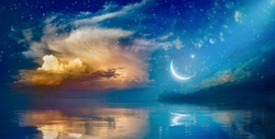 Ramadan Kareem background with crescent, stars and glowing clouds above serene sea.  Elements of this image furnished by NASA