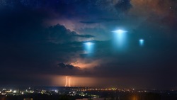 Amazing fantastic background - extraterrestrial aliens spaceship fly above small town, ufo with blue spotlights in dark stormy sky. Elements of this image furnished by NASA